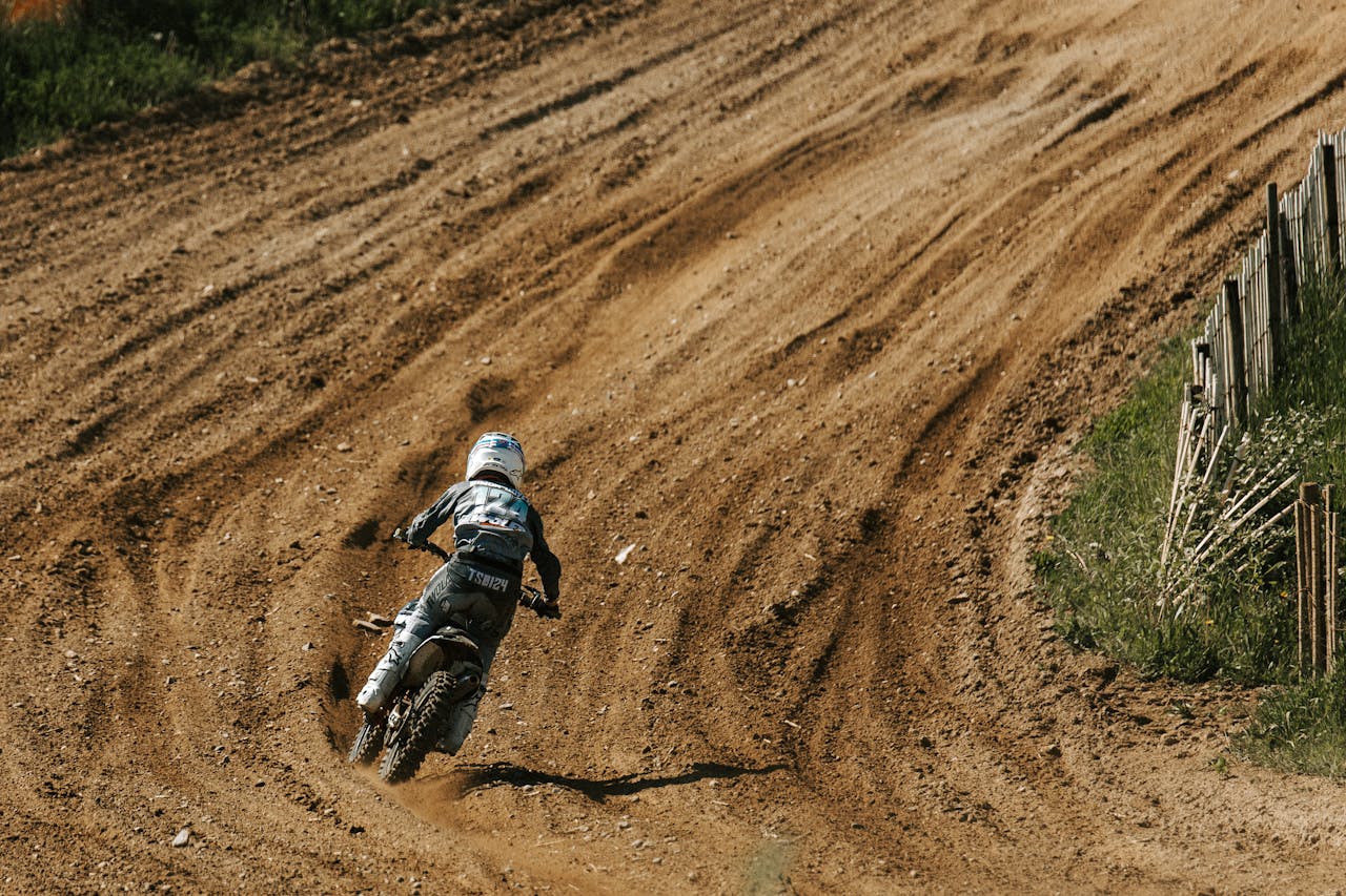 Motocross rider in action racing on a dirt track during a sunny day.